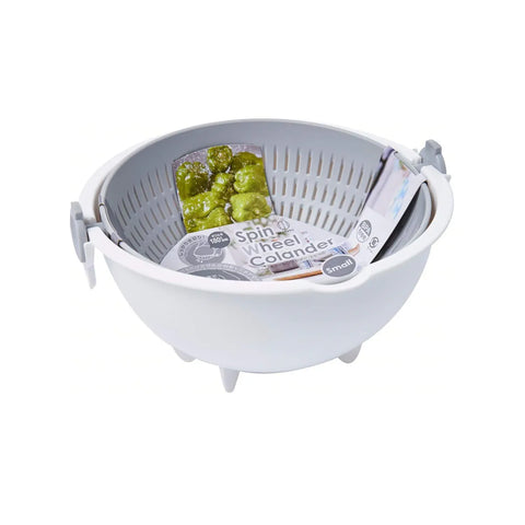 A white plastic spin-and-wheel colander basket with a gray interior, shown on a clean white background. Inside the basket are packaged food items, including a green pickle jar and a packet of Spin & Wheel Colander.