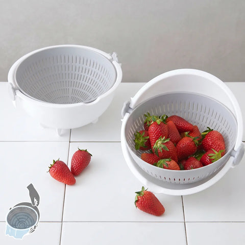 A white plastic strainer basket with a lid and side handles, shown empty and filled with red strawberries on a white tiled surface against a light gray wall.