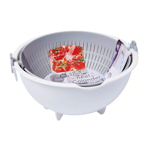 A white plastic spin wheel colander with a gray interior basket, shown on a plain white background with a tomato slice and packaged ingredients inside to demonstrate use.