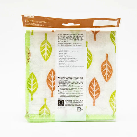 A packaged kitchen towel with a white background and a pattern of green and orange leaves, sealed in a clear plastic bag with a brown header card.