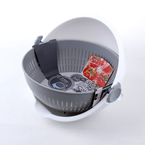 A gray and white plastic salad spinner basket with a white outer bowl and gray perforated inner basket, shown on a white background with a tomato and a circular insert visible inside.