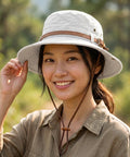 Woman wearing a light-colored bucket hat with a brown strap in an outdoor setting