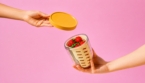 Person holding a container with strawberries against a pink background