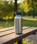 Metal water bottle with dark gray cap on a wooden bench in a park setting