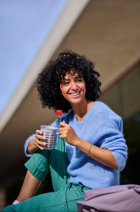 Woman holding a food container cup with a fork outdoors