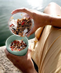 Person pouring granola into a bowl by a body of water