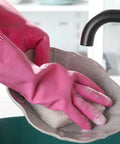 Pink cleaning glove scrubbing a dish with soap in a sink.
