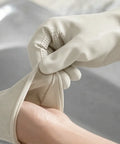 Close-up of hands wearing beige rubber gloves against a neutral background