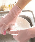 Person wearing pink gloves washing a bowl with a sponge in a sink.