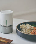 White cylindrical food dehydrator on a table next to a bowl of food