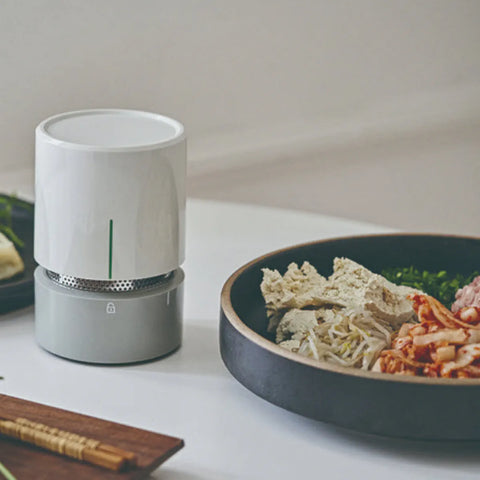 White cylindrical food dehydrator on a table next to a bowl of food