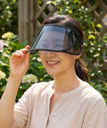 Woman wearing a visor with transparent face shield in front of greenery outdoors