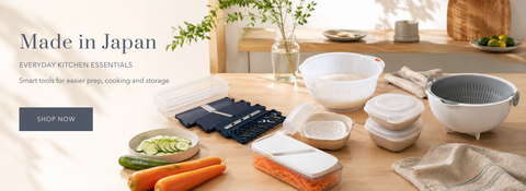 A collection of white and gray kitchen utensils and containers arranged on a wooden table, with vegetables nearby and a banner reading 'Made in Japan' on the left.