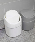 Two trash bins, one white and one gray, on a speckled countertop.