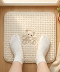 Person wearing white socks on a textured mat with a teddy bear design on a wooden floor.