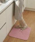 Person standing on a pink bath mat in a kitchen
