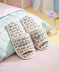 Pair of checkered slippers on a bed with a colorful pillow and flowers in the background