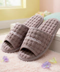 Pair of brown textured slippers on a light pink surface with flowers around.