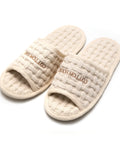 Pair of beige slippers with textured surface and 'Cotton House' branding on a white background