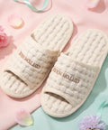 Pair of beige slippers with 'Cotton House' branding on a pink and green background with flowers.