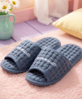 Blue slippers with 'Cotton House' branding on a pink surface, with a vase of flowers in the background.