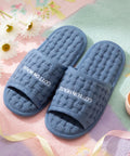 Pair of blue slippers with 'Cotton House' branding on a floral background