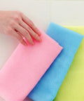 Three colorful sponges (pink, blue, yellow) on a white background with a hand touching the pink sponge.