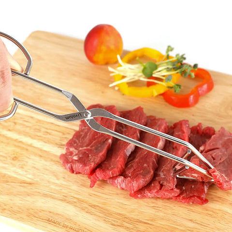 Stainless steel triangle tongs gripping cuts of raw beef on a wooden cutting board.