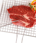 Raw beef on top of metal grill grates and plating tongs pinching the steak.
