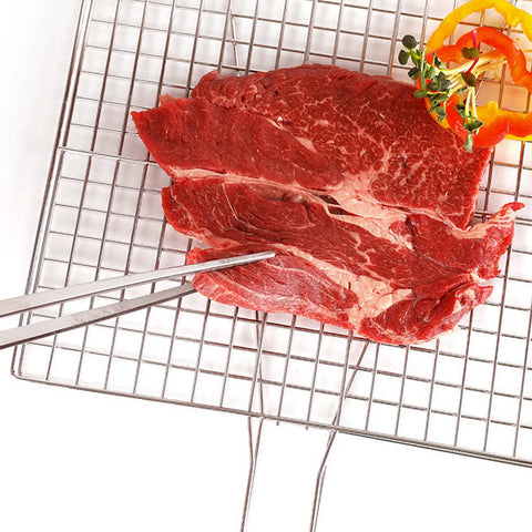 Raw beef on top of metal grill grates and plating tongs pinching the steak.