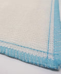 A close-up of a white woven fabric with a light blue stitched border, showing the texture of the material.