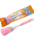 A pink sponge cleaning brush with a white handle and orange-and-blue retail packaging, photographed on a plain white background.