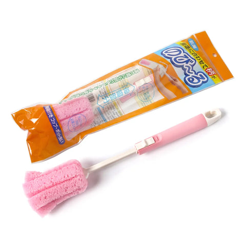 A pink sponge cleaning brush with a white handle and orange-and-blue retail packaging, photographed on a plain white background.