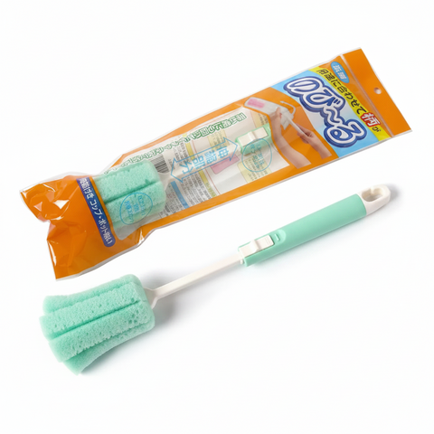 A mint green and white sponge cleaning brush with a white handle is shown in front of its orange and blue retail packaging on a white background.