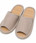 A pair of open-toe slip-on slippers with a beige woven fabric upper and a light tan bamboo-look footbed, shown on a plain white background.