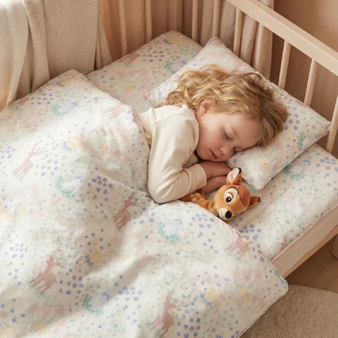 Child sleeping in a crib with a patterned comforter and pillow, holding a stuffed animal.