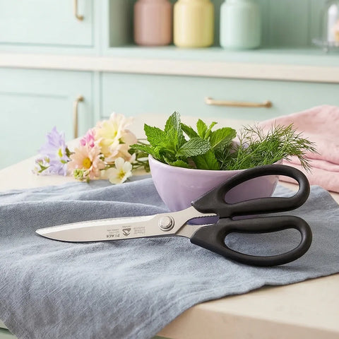 Scissors on a kitchen counter with a bowl of herbs and flowers in the background.