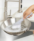 Person cleaning a frying pan with a brush in a kitchen setting