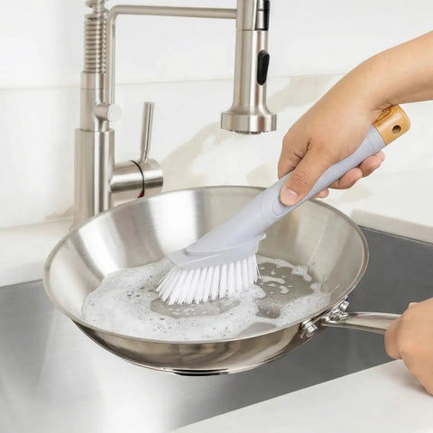 Person cleaning a frying pan with a brush in a kitchen setting