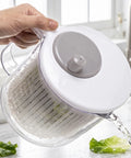 Hand using a salad spinner with lettuce on a kitchen counter