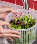 Person washing greens in a colander under running water from the kitchen sink