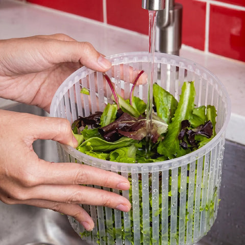 Person washing greens in a colander under running water from the kitchen sink