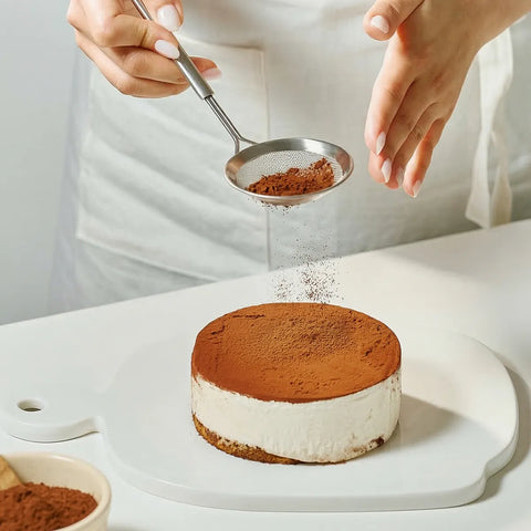 Person dusting cocoa powder over a dessert on a white surface
