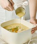 Person ladling soup into a bowl with a white background