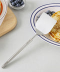 Stainless steel turner resting on a plate of pancakes on a white tabletop