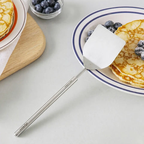 Stainless steel turner resting on a plate of pancakes on a white tabletop
