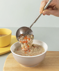 Person ladling soup into a bowl with a spoon on a wooden surface.