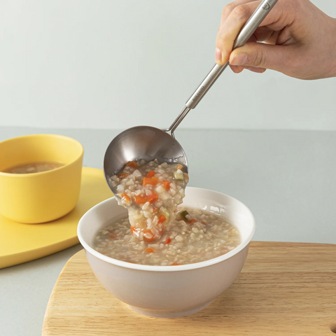Person ladling soup into a bowl with a spoon on a wooden surface.