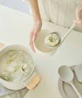 Person holding a bowl of soup and a ladle with a dumpling in it with a neutral background