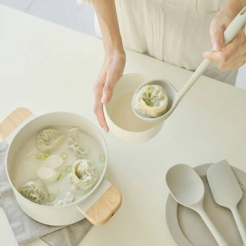 Person holding a bowl of soup and a ladle with a dumpling in it with a neutral background